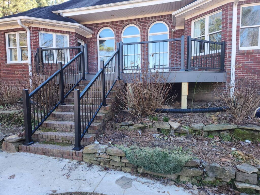 Raised custom deck with black railings and stairs beside a brick home by Elite Decks, deck builder serving Calera, AL
